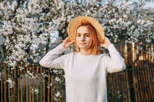 Portrait of a woman in a straw hat in a cherry blossom. Free outdoor recreation, spring blooming garden.