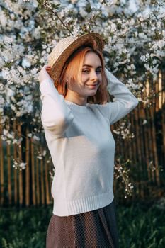 Portrait of a woman in a straw hat in a cherry blossom. Free outdoor recreation, spring blooming garden.