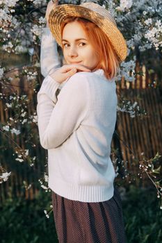 Portrait of a woman in a straw hat in a cherry blossom. Free outdoor recreation, spring blooming garden.