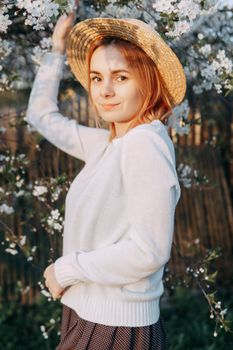 Portrait of a woman in a straw hat in a cherry blossom. Free outdoor recreation, spring blooming garden.