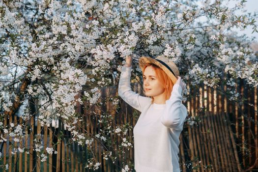 Portrait of a woman in a straw hat in a cherry blossom. Free outdoor recreation, spring blooming garden.