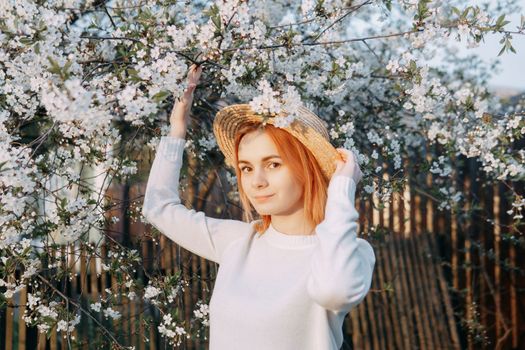 Portrait of a woman in a straw hat in a cherry blossom. Free outdoor recreation, spring blooming garden