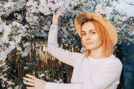 Portrait of a woman in a straw hat in a cherry blossom. Free outdoor recreation, spring blooming garden.