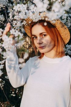 Portrait of a woman in a straw hat in a cherry blossom. Free outdoor recreation, spring blooming garden.