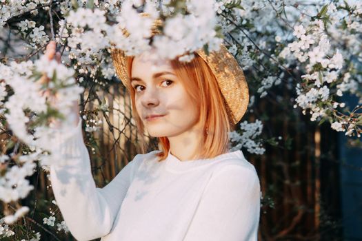 Portrait of a woman in a straw hat in a cherry blossom. Free outdoor recreation, spring blooming garden.