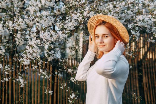 Portrait of a woman in a straw hat in a cherry blossom. Free outdoor recreation, spring blooming garden.