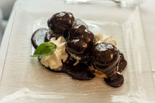 Traditional french chocolate-coated profiteroles with whipped cream and mint