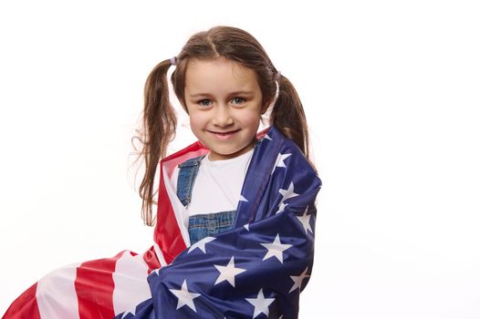 Beautiful little citizen of United States of America, a lovely baby girl with two ponytails, wrapping USA flag, isolated over white background. Citizenships. Independence Day. Immigration concept