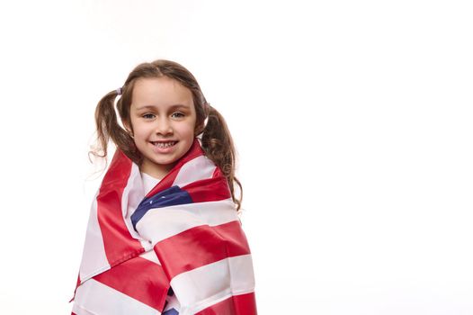 Lovely preschooler girl with two cute ponytails, wrapping in USA flag, celebrating the independence Day of United States of America on July 4 th. Concept of human rights and freedoms. White background