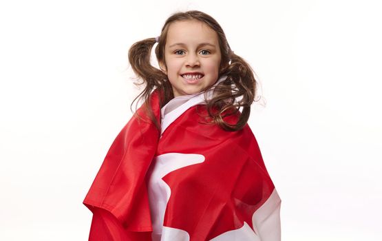 American lovely little child girl, Canadian citizen wrapping flag of Canada, smiling a beautiful toothy smile looking at camera, isolated on white background. Copy ad space. Dominion Day. 1st July