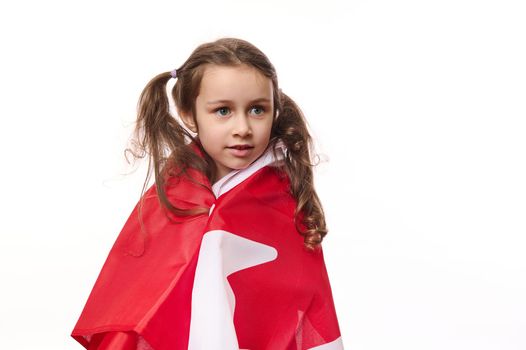Canadian citizen, a lovely little girl with two ponytails, wrapping Canadian flag, isolated over white background, free space for advertising space. Citizenships. Independence Day. Immigration concept