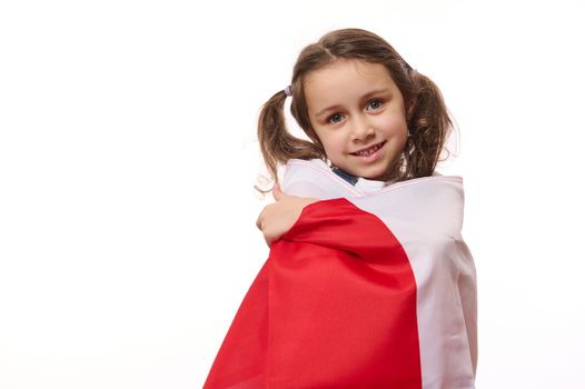 Isolated portrait on white background of a beautiful little child girl, proudly wrapping in flag of Poland or Canada. Concept of national holidays and patriotic events. Patriotism. Independence Day