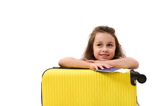 Adorable little passenger girl, with boarding pass and suitcase, traveling abroad for the weekend, smiling toothy smile, dreamily looking away at advertising space. Tourism Tourney Air travel concept