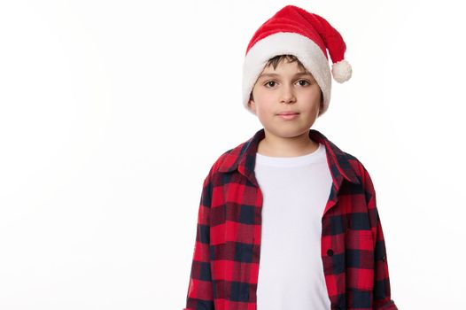 Half-length portrait of handsome Caucasian teenage boy in Santa hat, looking confidently at camera, isolated on white background. Copy space for advertising text. Merry Christmas and Happy New Year