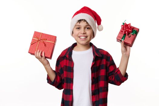 Adorable Caucasian preteen boy in Santa hat, in anticipation of winter holidays, excited about gift, isolated on white background with copy ad space. Time to open Christmas presents. Xmas atmosphere