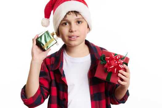 Half-length portrait: handsome Caucasian teenage boy in Santa hat, holding Christmas gifts, looking confidently at camera, isolated on white background. Copy space for advertising text. Happy New Year