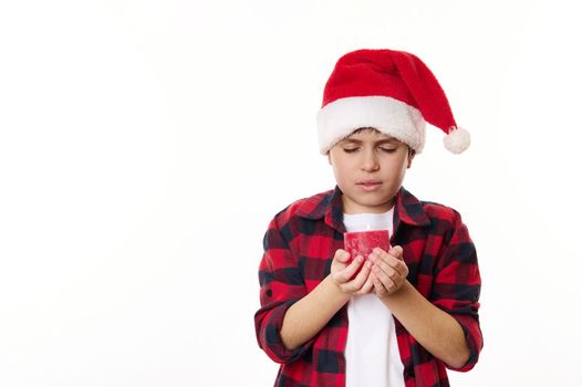Half-length portrait of a child boy in Santa hat, holding a red lit candle, making wish for Christmas, isolated on white background with copy advertising space. Magical atmosphere of winter holidays