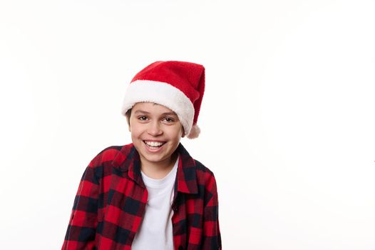 Isolated portrait on white background, with copy advertising space, of a charming teenage boy in red Santa hat, laughing and smiling a cheerful toothy smile looking at camera. Facial expressions