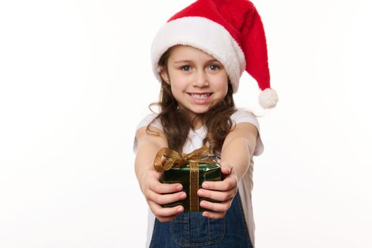 Selective focus on hands of a blurred lovely little girl in Santa hat, holding a cute Christmas present, isolated on white background. Copy space. Christmas Eve. New Year and winter holidays concept