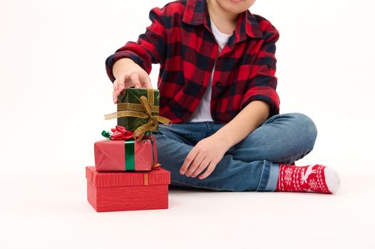 Selective focus on beautiful happy presents folded one on one, on a white background, next to a teenage boy in red plaid shirt and socks with Christmas pattern. Boxing Day. Xmas. New Year celebration