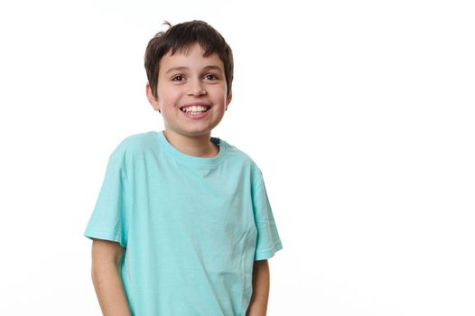 Emotional portrait of Caucasian cheerful teenage boy wearing turquoise t-shirt, smiling a beautiful toothy smile looking at camera, isolated on white background. Copy space for your promotional text