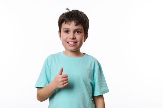Emotional portrait of lovely Caucasian teen boy, showing thumb up, smiling looking at camera, isolated on white background with copy space for promotion. Smart schoolboy, teenager, pre-adolescent boy