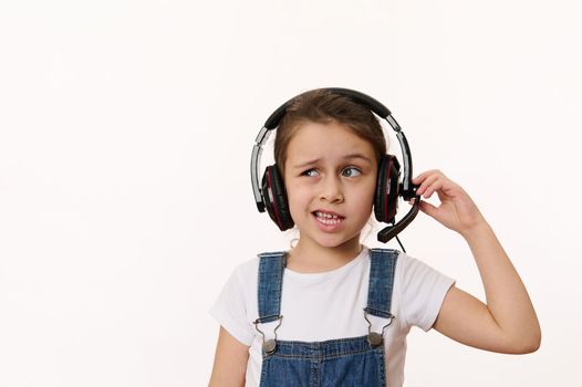 Adorable little child, smart school girl wearing headphones has a video conference during an online lesson, isolated over white background. Copy advertising space. Back to school. Internet learning