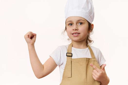 European beautiful little girl - chef pastry, cook, baker confectioner wearing kitchen apron and hat, isolated on white background with free space for promotional text. Cooking class for talented kids