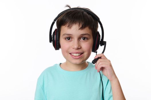 Close-up portrait of a handsome Caucasian smart teenage school boy, wearing audio headset, ready for online lesson, smiling cutely looking at camera, isolated over white background. Copy ad space