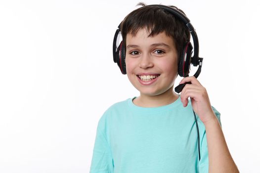 Beautiful smart little school girl, first grader wearing audio headset, ready for online lesson, smiling cutely looking at camera, isolated over white background with copy advertising space for text