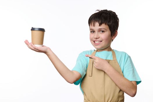 Adorable teenage boy, barman barista bartender wearing beige chef's apron, selling giving making a takeaway coffee in cardboard cup. Hot beverage drink to go, isolated on white background. Copy space