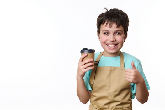 Happy Caucasian teenage boy, bartender barista holding, selling a takeaway hot coffee drink in a paper cup, showing thumb up, isolated over white background with copy space for your promotional text