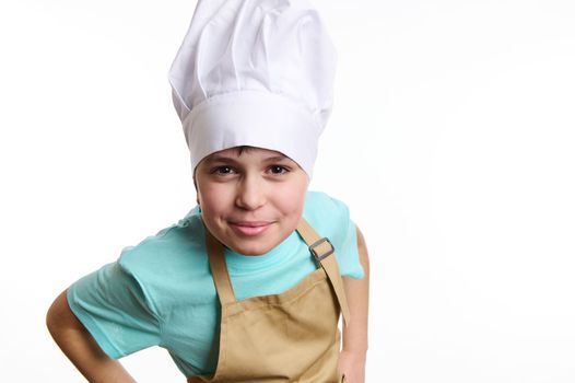 Close-up of an overjoyed happy pre-adolescent child- chef pastry, cook, baker confectioner wearing chef hat and beige apron, isolated on white background. Free ad space. Culinary and bakery concept