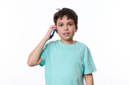 Happy multi-ethnic teenage boy wearing blue t-shirt, talking on mobile phone, isolated over white background with copy advertising space