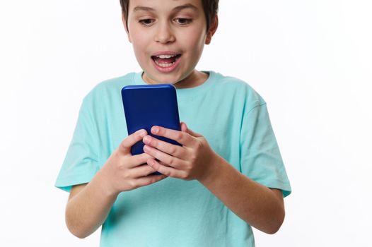 Selective focus on mobile phone in the hands of a teenager boy, expressing surprise while using smartphone, browsing websites, scrolling news feed, checking social media content, isolated on white