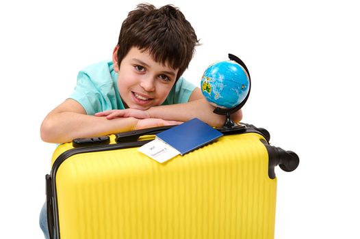 Close-up portrait of a happy teenage boy passenger with yellow suitcase and globe, cutely smiles looking at camera, isolated over white background. Travel. Tourism. Journey concept Free ad space