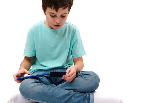 Close-up teenage boy holding credit card and smartphone, buying via internet, isolated over white background. Copy advertising space. Online payment. Money transfer. Internet banking. Transaction