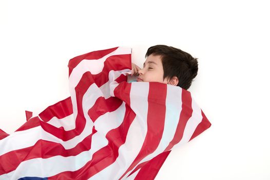 Serene multi-ethnic child boy wrapped in USA flag, isolated on white background. Concept of love for the motherland, citizenships, social secure, patriotism and freedom. Independence Day on July 4th