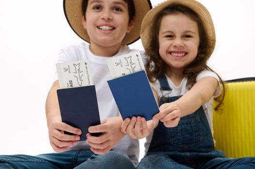 Selective focus on flight ticket or boarding pass in blurred traveler passenger kid's hands near a yellow suitcase over white background. Travel. vacations. Journey. Flight. Space for advertising text