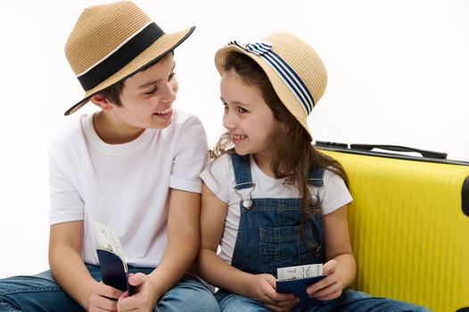 Happy travelers kids with yellow suitcase and air tickets, going for summer vacation. Little girl and teenage boy, sister brother, traveling abroad for weekend getaway, isolated over white background