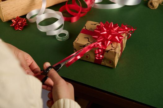 Overhead view woman's hands tying beautiful bow from shiny red ribbon while decorating a Christmas or New Year's present. Wrapping presents for New Year or any other celebration event. Boxing Day
