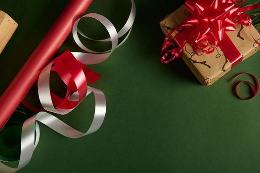Flat lay. Still life. Christmas present, wrapping paper with deer pattern and shiny decorative ribbons for tying up gifts, isolated on a green background. Copy advertising space. Mockup. Boxing Day