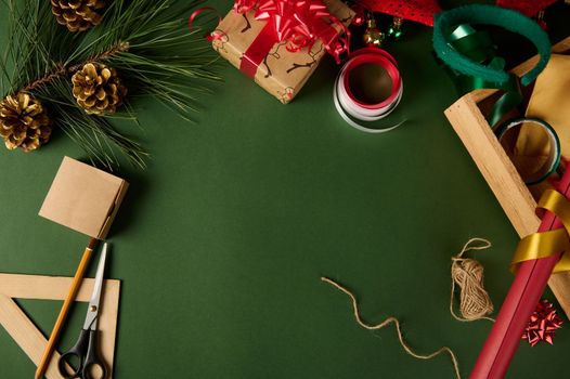 Christmas background with copy advertising space. Beautiful gifts with wrapping materials, decorative tapes, rope, golden pine cones and evergreen fir-tree branch on green surface. Boxing Day. Mockup