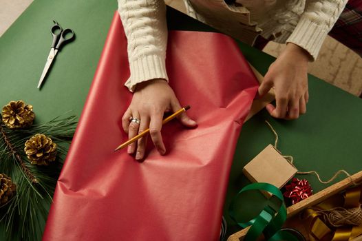 Close-up. View from above of woman's hands calculate the amount of wrapping paper for packing Christmas, New Year's or Saint Valentine's Day gifts, at green background. Boxing Day. Diy. Handwork art