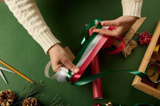 Top view woman's hands choose decorative shiny tapes for tying up presents, over a background with wrapping materials, for packing gifts for Christmas, New Year or other celebration event. Boxing Day