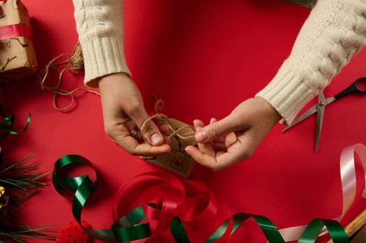 Top view craftswoman wrapping Christmas present in a decorative gift paper with deer pattern, tying a bow with craft linen rope. Boxing Day. Packing. Tying up gifts. Xmas and New Year preparations