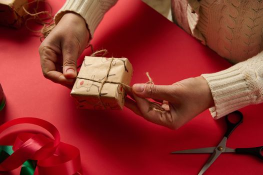 Directly above Craftswoman wraps Christmas present in a wrapping paper with deer pattern, tying a bow with craft linen rope. Boxing Day. Packing. Tying up gifts. Xmas and New Year preparations