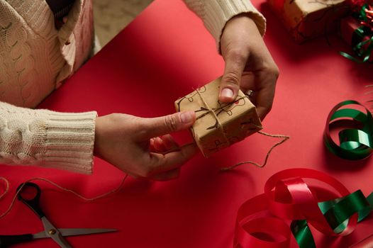 Craftswoman tying up a Christmas gift in a wrapping paper with deer pattern, tying bow using a linen rope. Boxing Day. Diy presents. New Year preparations. Step by step packing presents. Festivity