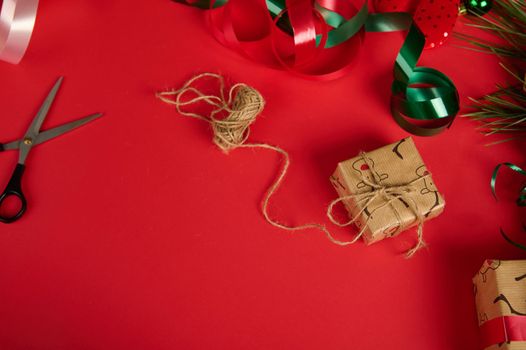 Christmas or New Year presents, wrapped in a wrapping paper with deer pattern and tied up with linen rope, laid out green shiny tape, isolated over a red background with copy ad space. Packing gifts.