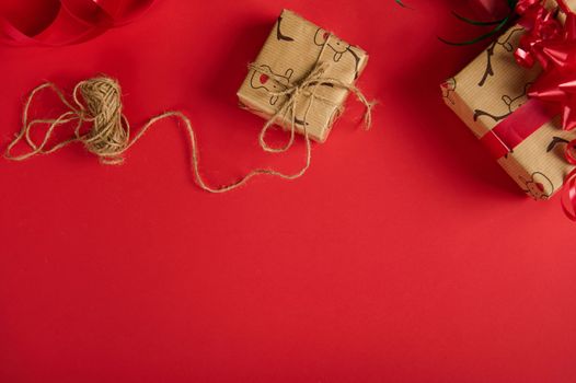 Beautiful presents, wrapped in a wrapping paper with deer pattern and tied up with linen rope and red tape, on top of a red background with copy advertising space. Christmas and New Year preparations